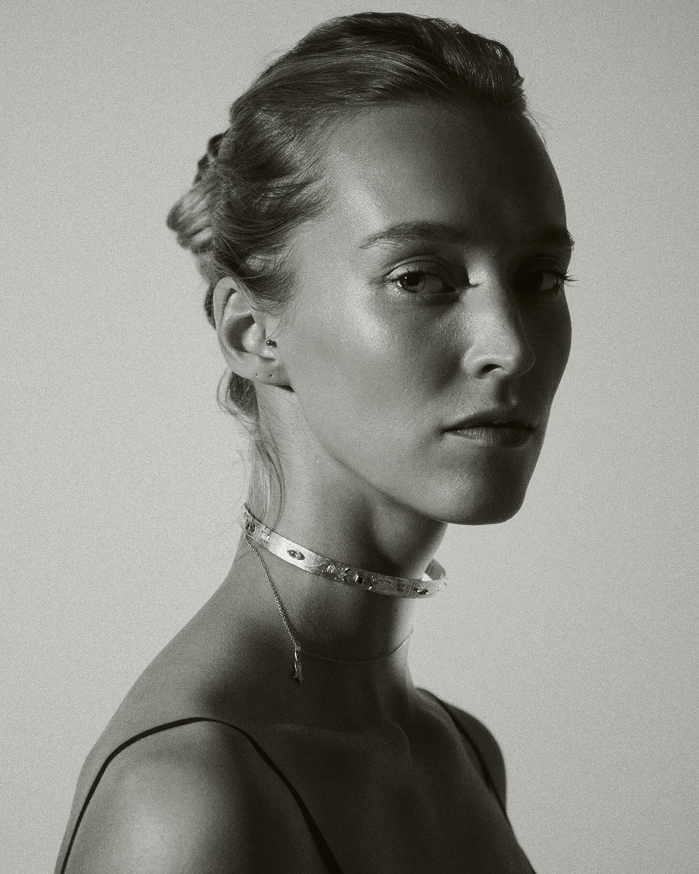 Black and white portrait of a woman wearing a delicate necklace against a plain background