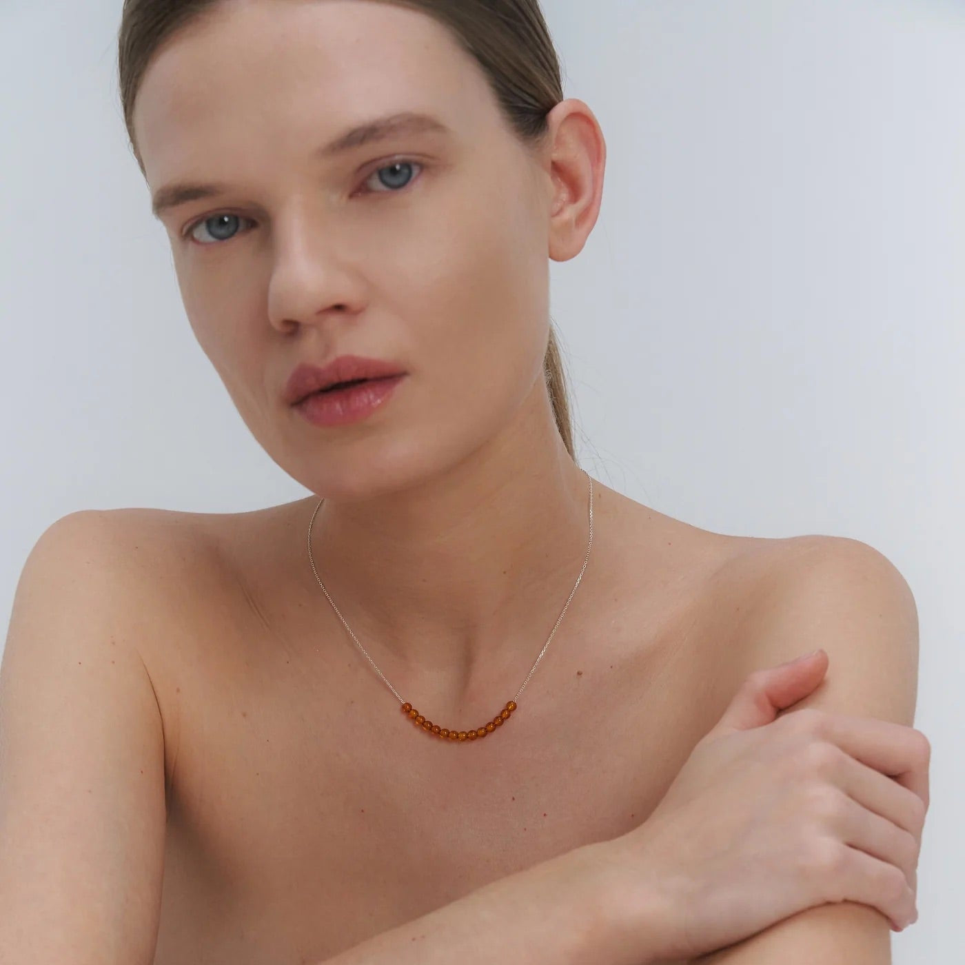 Woman wearing a silver necklace with Baltic amber beads against a plain background