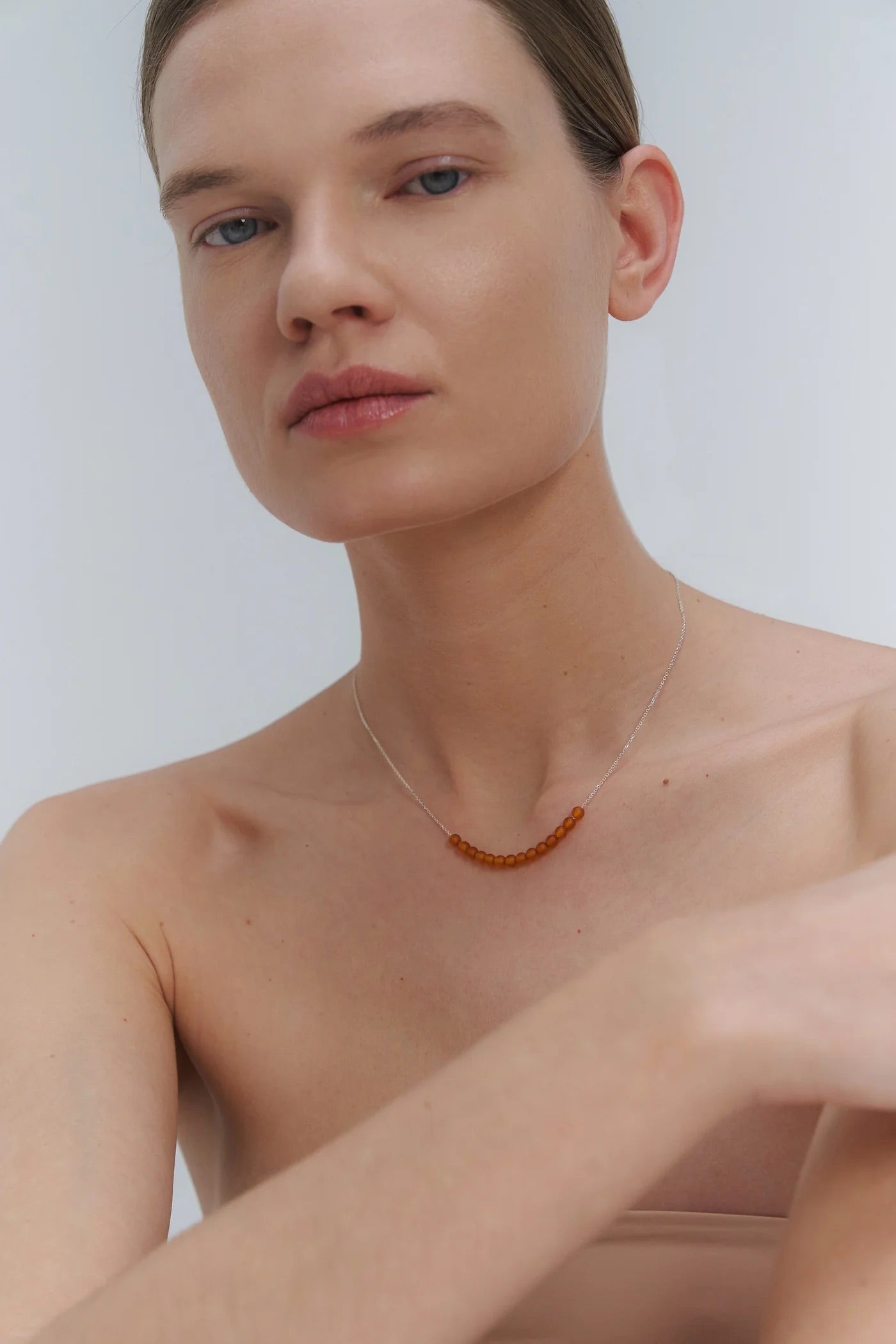 Woman wearing a silver necklace with Baltic amber beads against a plain background