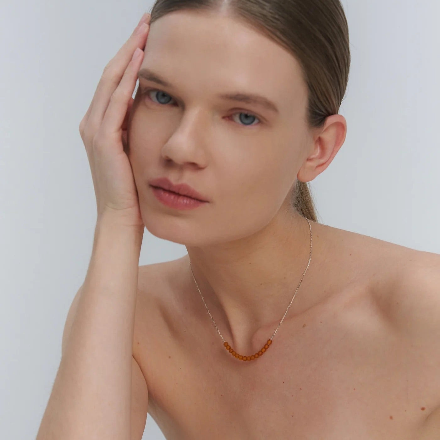 Woman wearing a silver necklace with Baltic amber beads against a plain background