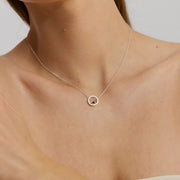 Necklace with a small round pendant on a person's neck against a neutral background