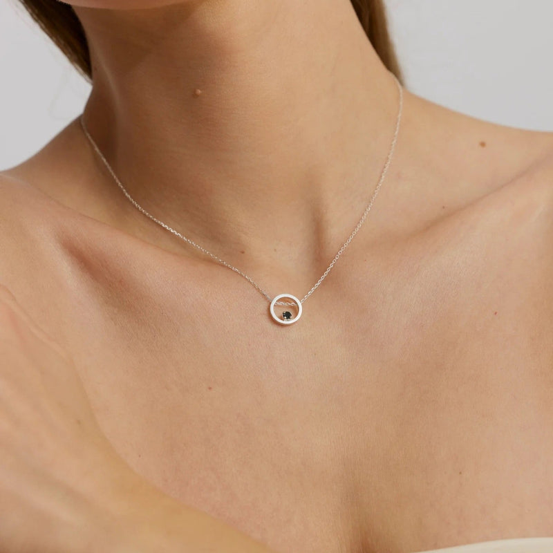 Necklace with a small round pendant on a person's neck against a neutral background