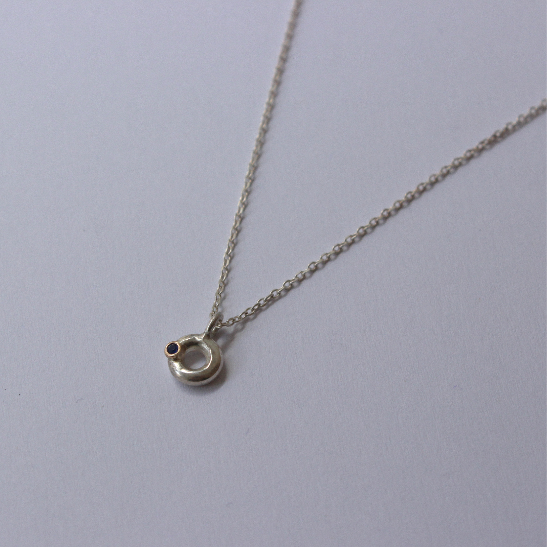 Silver necklace with a small blue sapphire pendant on a light gray background