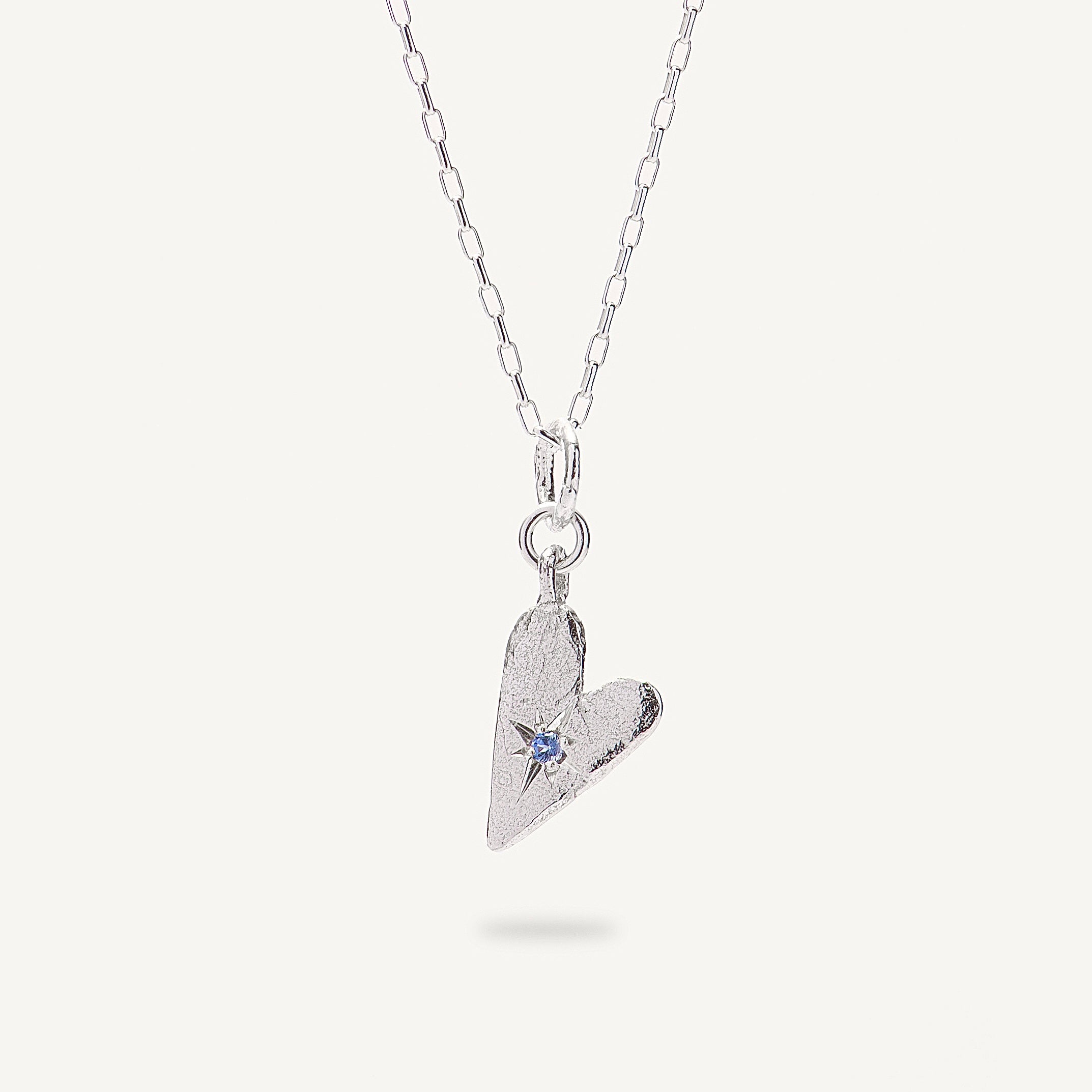 Silver heart-shaped pendant necklace with a blue gemstone on a white background