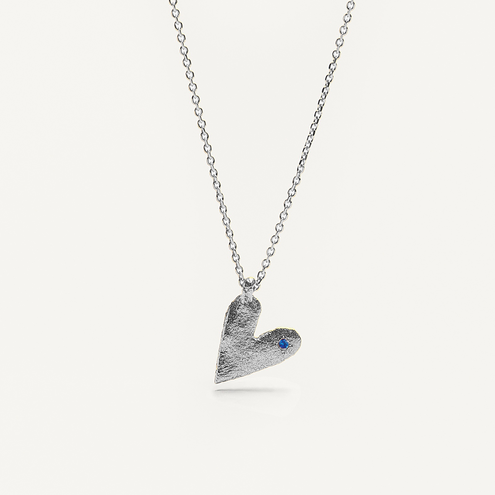 Silver heart-shaped pendant necklace with a blue sapphire on a white background