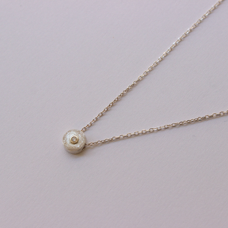 Delicate necklace with a small diamond pendant on a light gray background