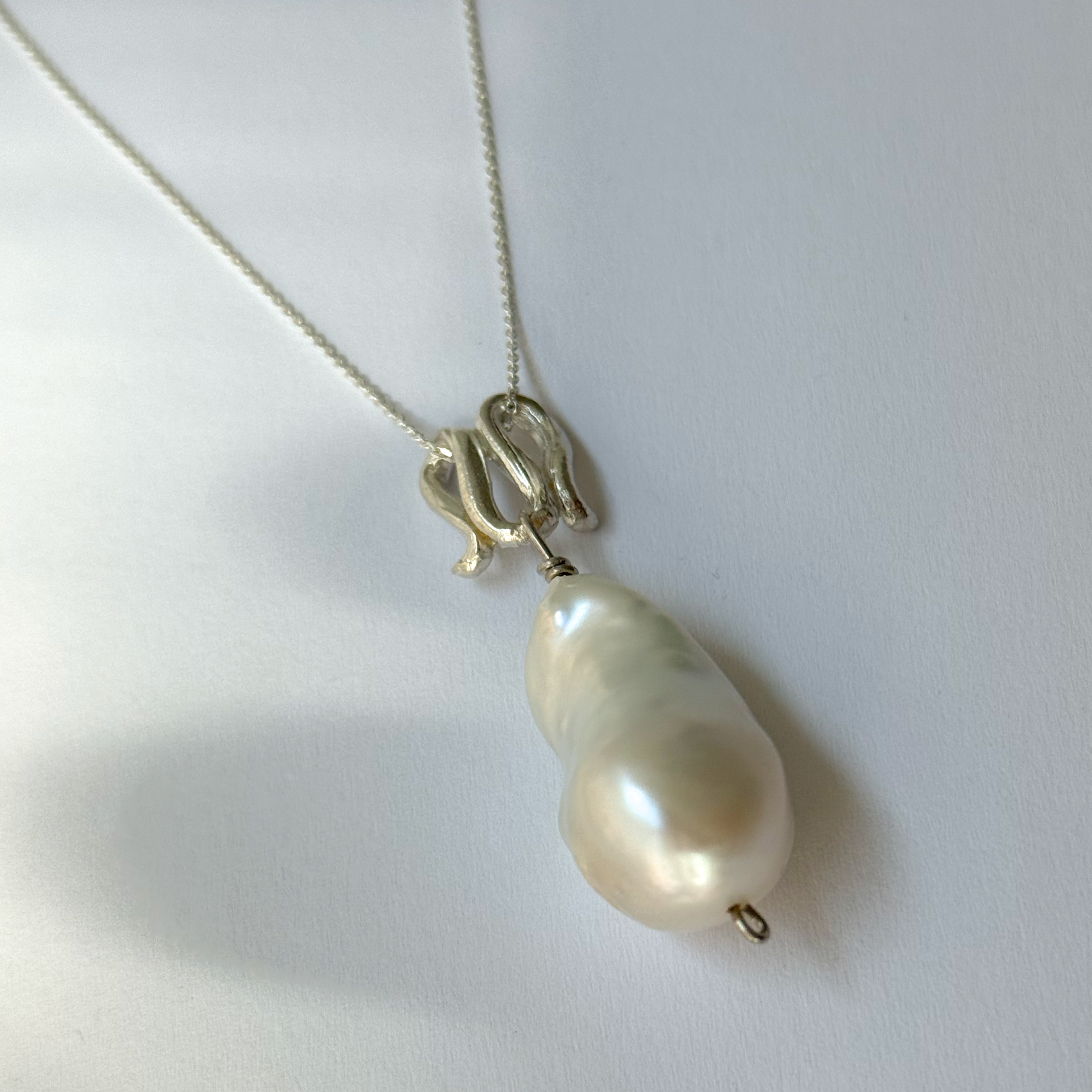 Infinity-shaped pendant featuring baroque shaped freshwater pearl. 