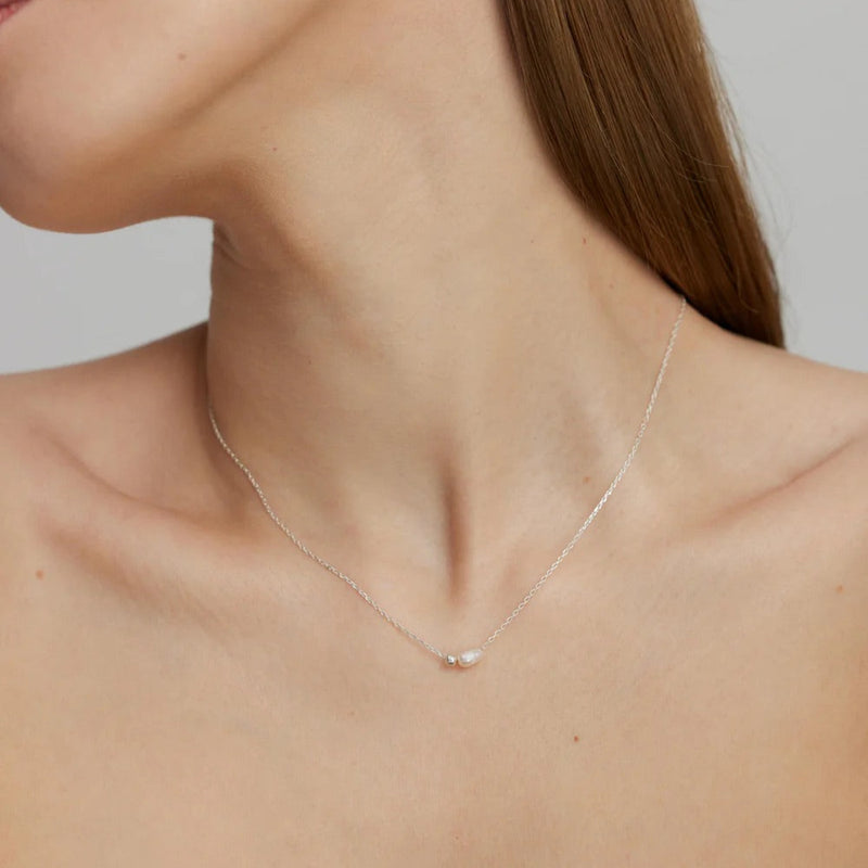 Silver necklace with a small pendant on a person's neck against a neutral background