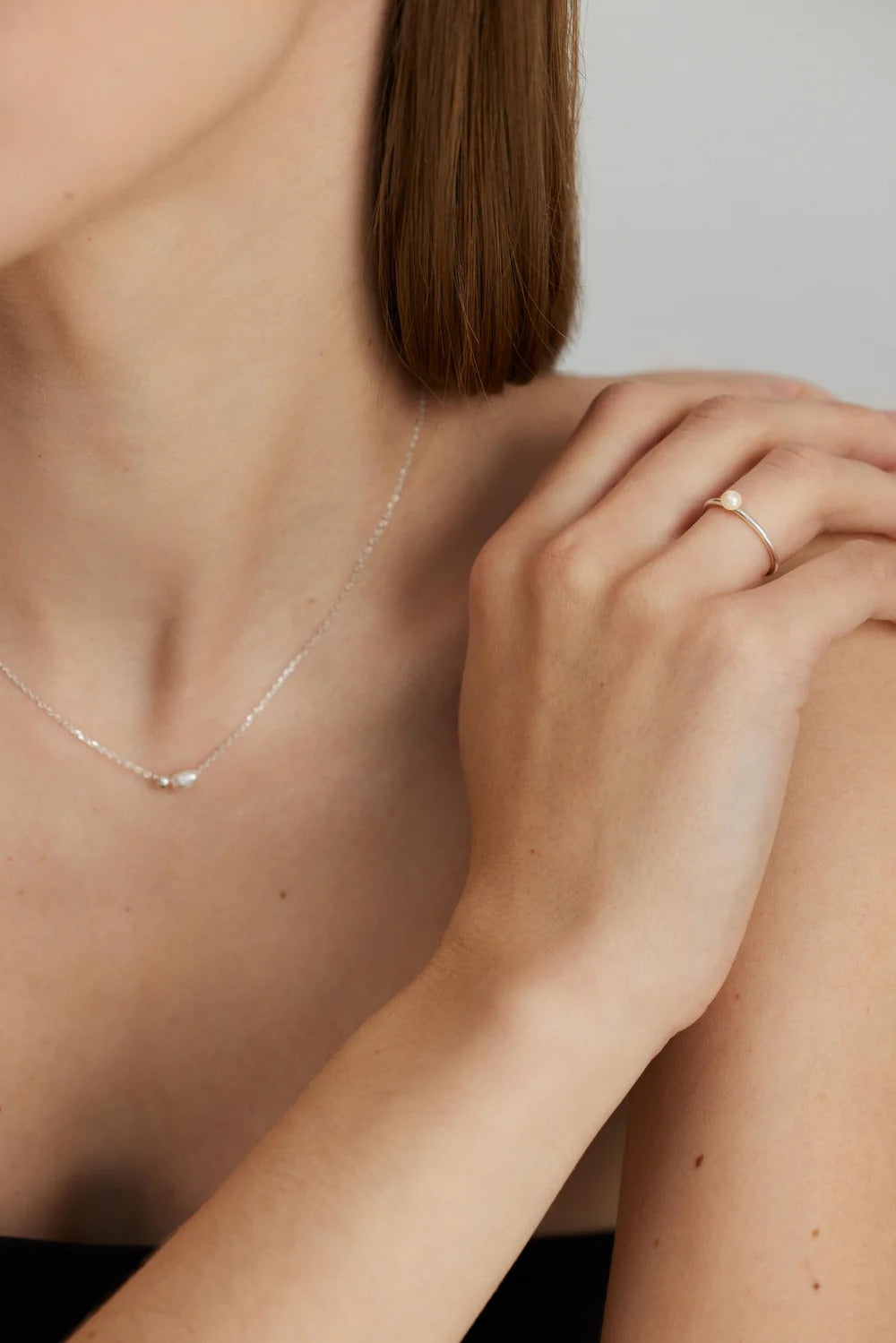 Close-up of a person wearing a delicate pearl necklace and ring on a neutral background