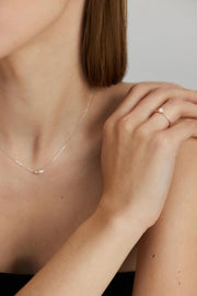 Close-up of a person wearing a delicate pearl necklace and ring on a neutral background