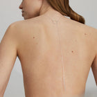 A person viewed from the back wearing a silver necklace with a straight, long chain and a ring, positioned on the back of the neck.