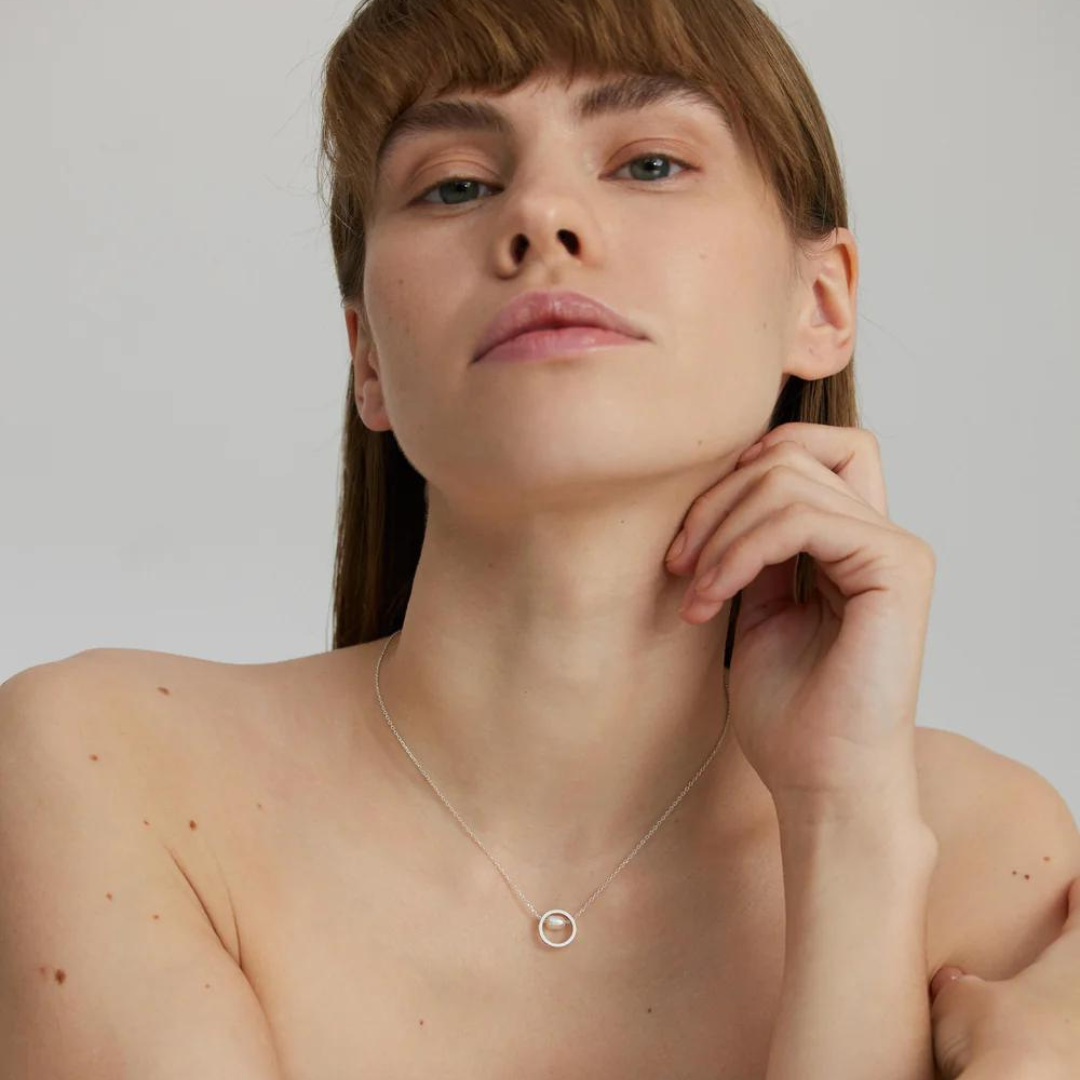 A woman wearing a silver necklace with a pearl in the center, presented on a model showcasing the piece.