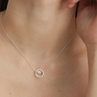A fine silver chain carries a small circular pendant, framing a single freshwater pearl suspended at its center. 