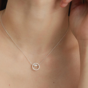 A fine silver chain carries a small circular pendant, framing a single freshwater pearl suspended at its center. 