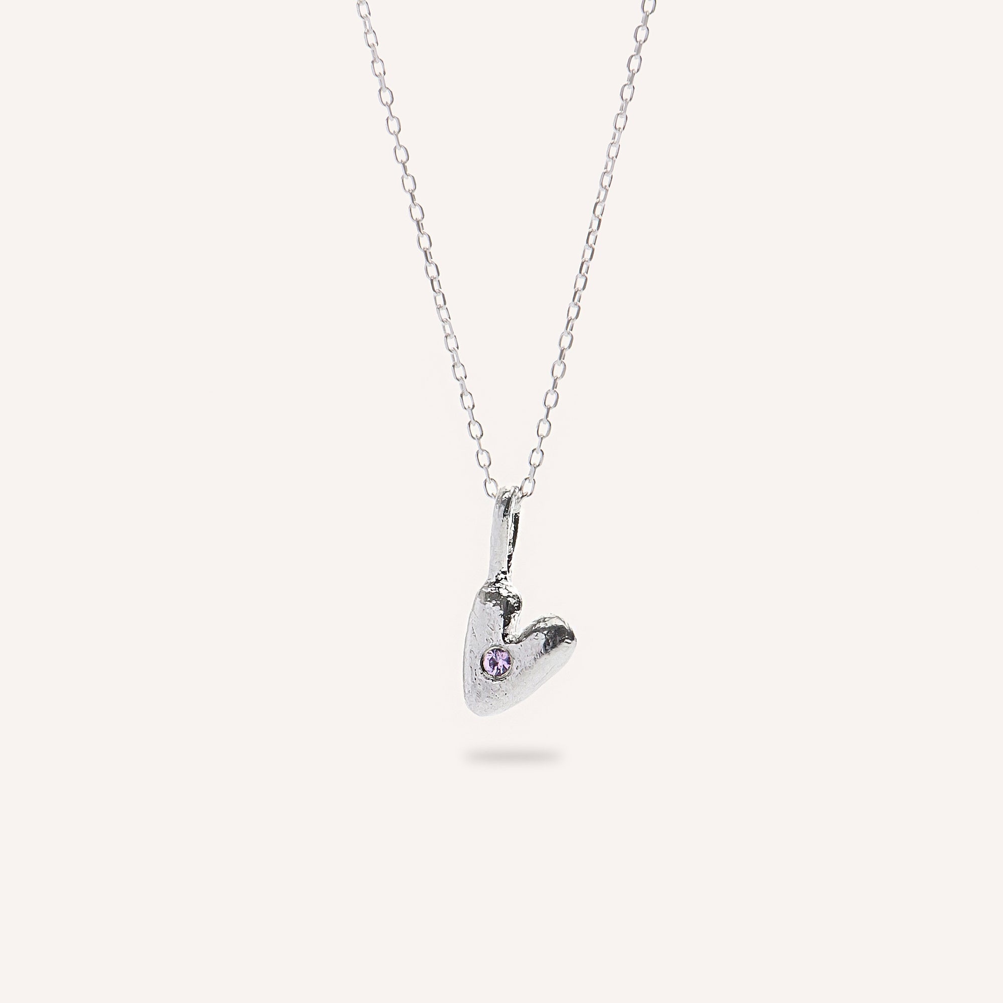 Heart-shaped silver pendant with a small gemstone on a white background