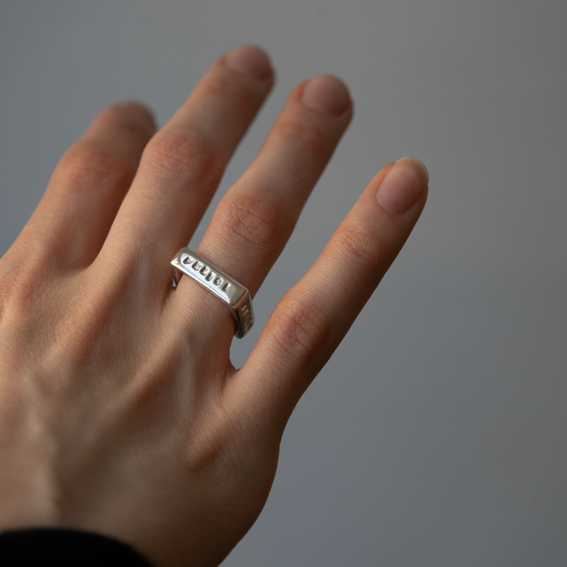 Hand wearing a silver ring with engraved text on a plain background