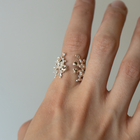 Hand wearing a silver ring with a floral design on a plain background