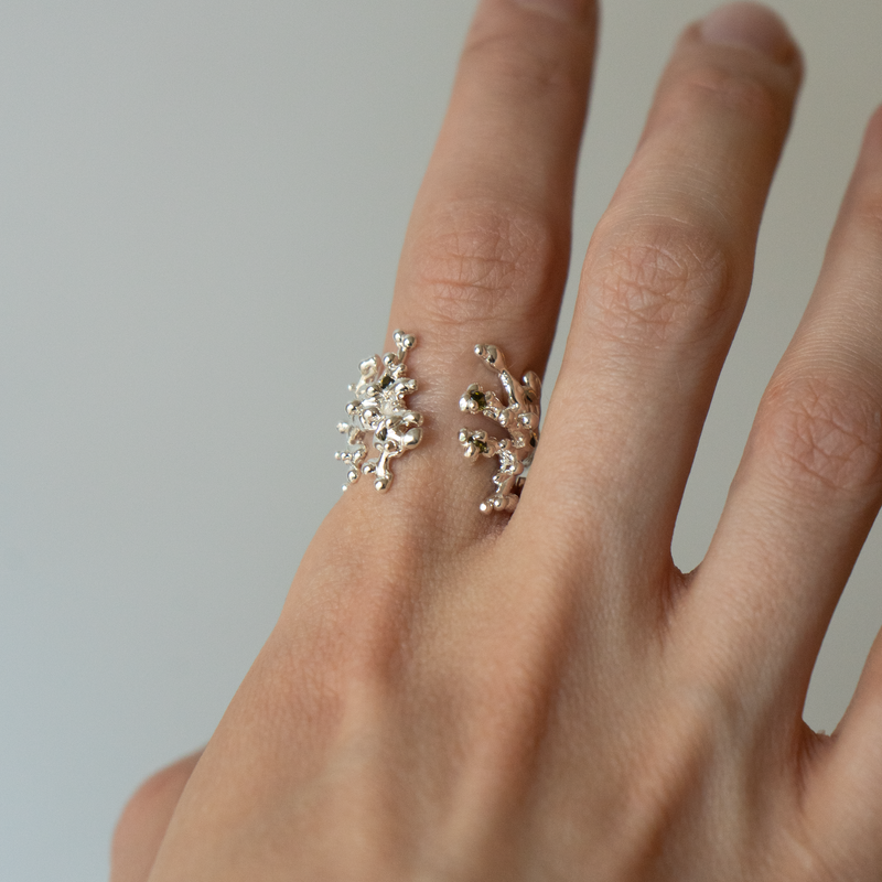 Hand wearing a silver ring with a floral design on a plain background
