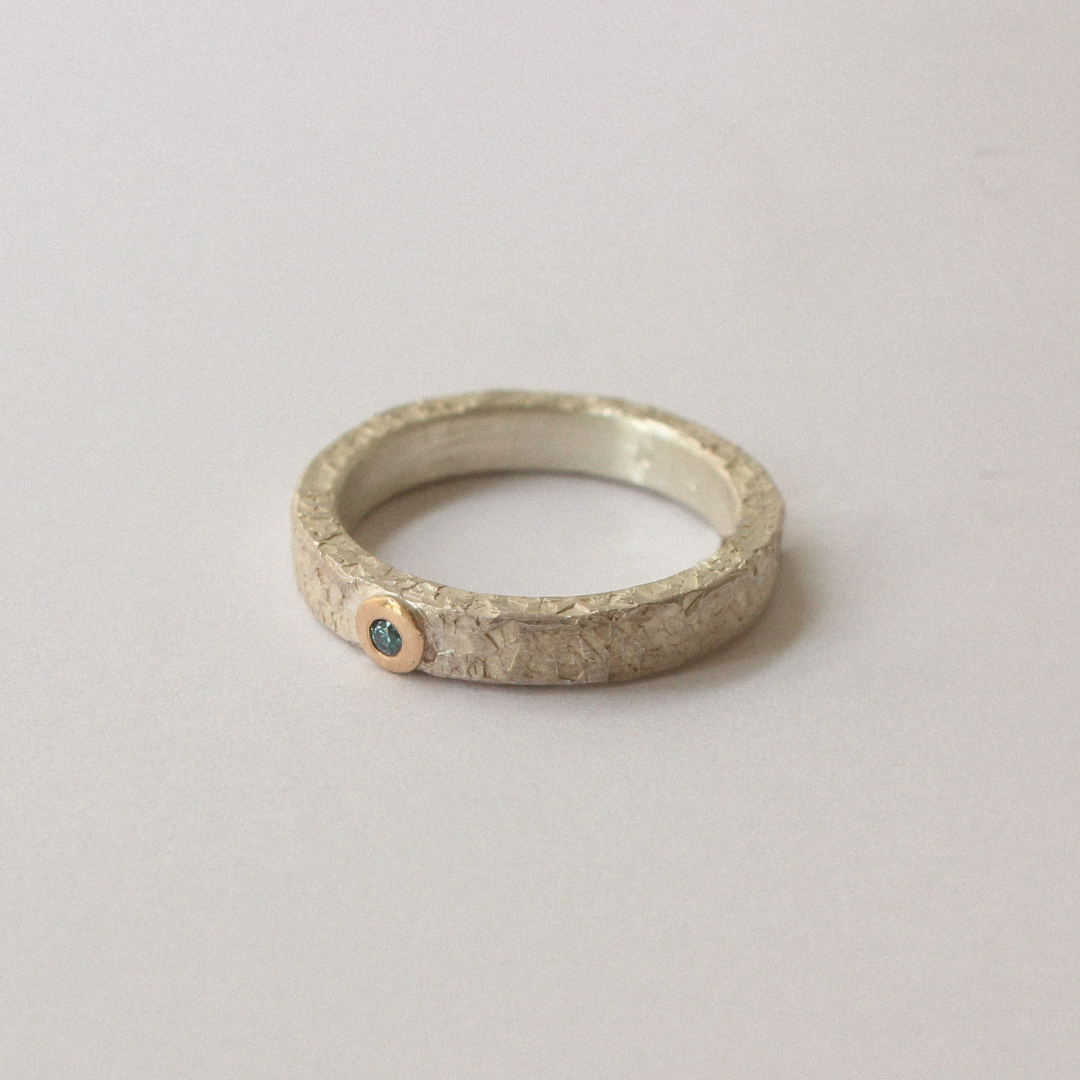 Silver ring with blue diamond on a light gray background