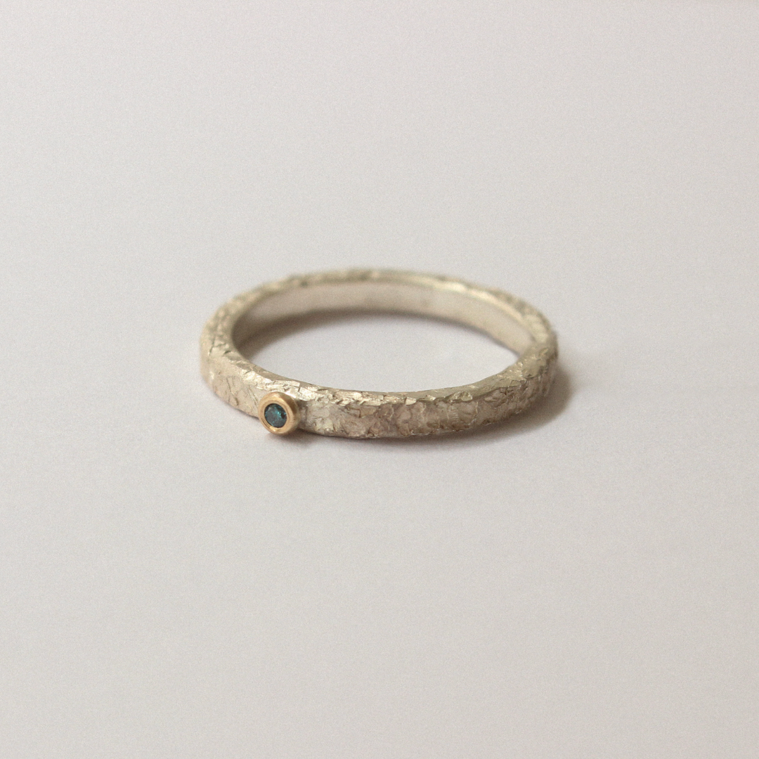 Silver ring with a blue diamond gemstone on a light gray background