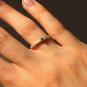 Hand wearing a gold ring with a blue diamond on a dark background