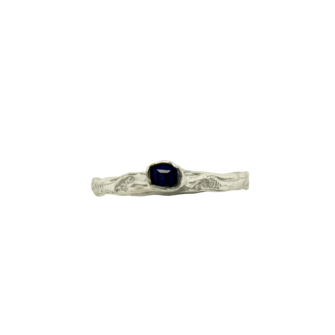 A silver ring with a sapphire stone set in a ornate setting, with a textured band and a narrow stone.