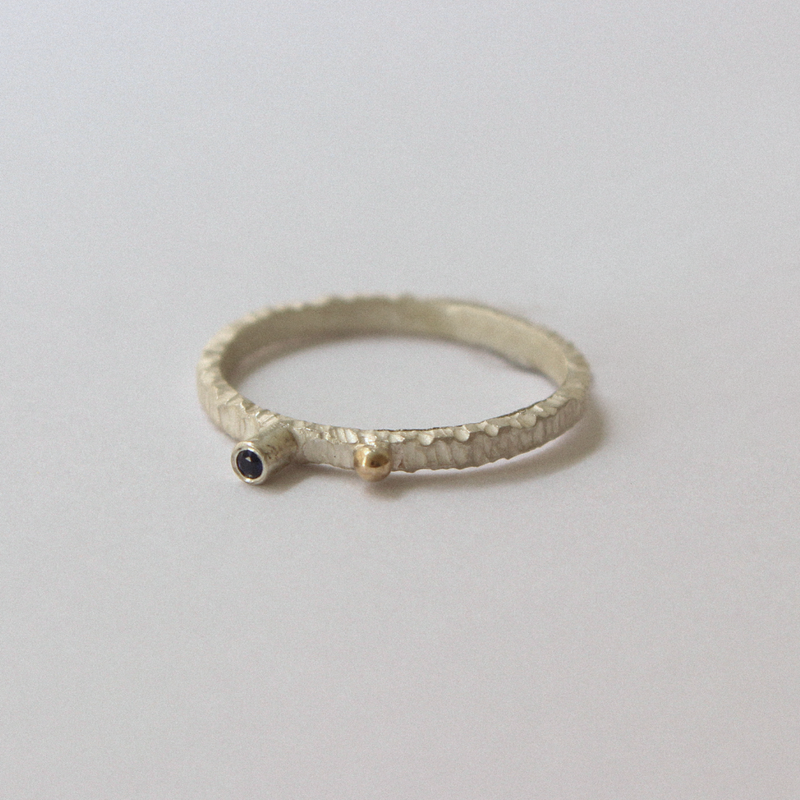 Silver ring with a gold accent and blue sapphire on a light gray background