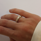 A close-up image of a hand holding a silver and diamond ring with a gold sphere decoration.