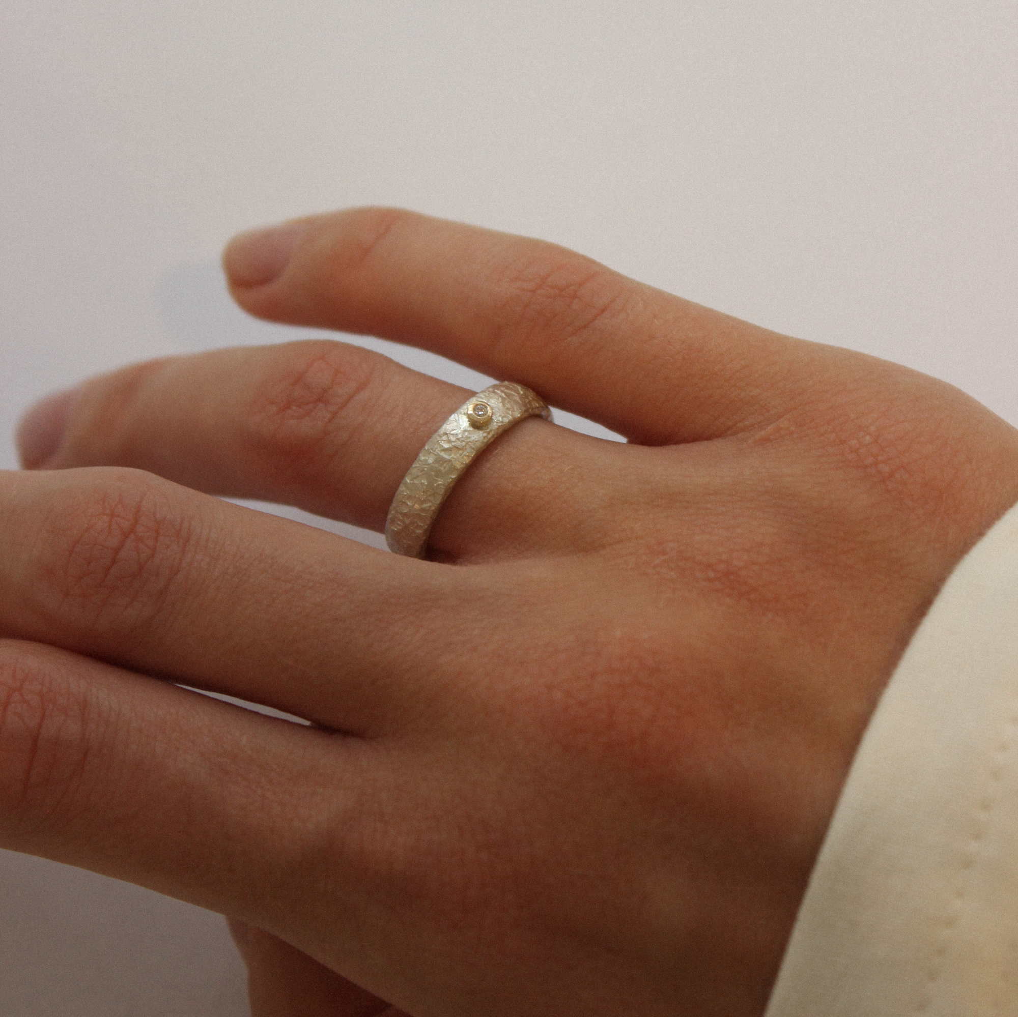 A close-up image of a hand holding a silver and diamond ring with a gold sphere decoration.
