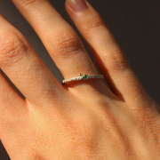 Close-up of a hand wearing a ring with a green emerald on a dark background