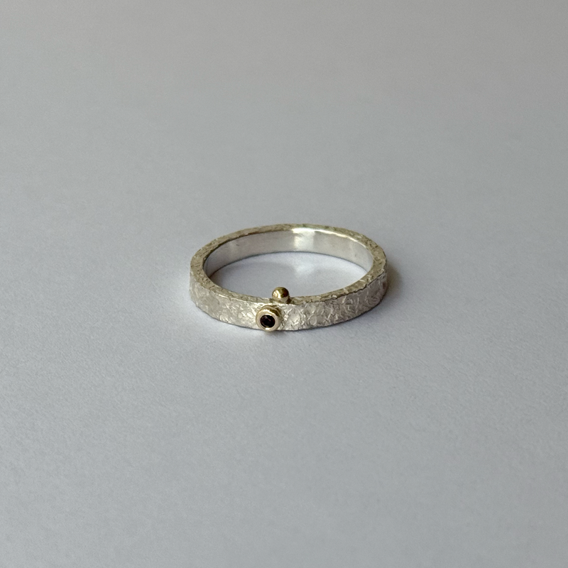 A silver ring with a red garnet in the center, decorated with gold bubbles, placed on a light background.