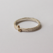 Silver ring with a small gold gemstone on a light gray background
