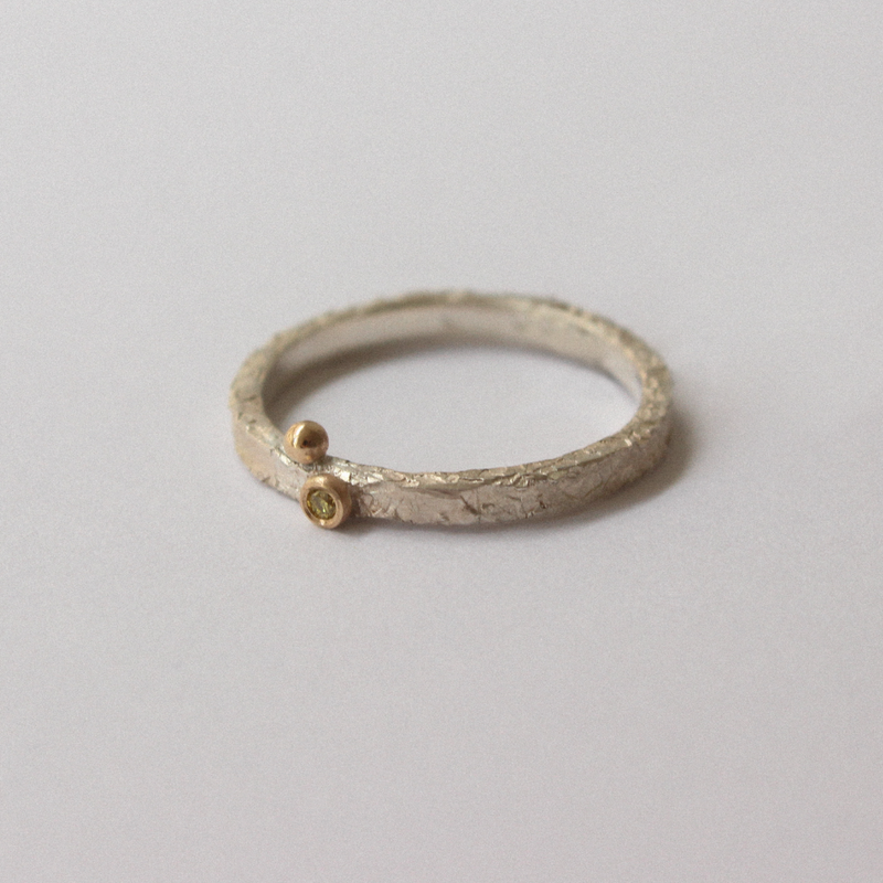 Silver ring with a small gold gemstone on a light gray background