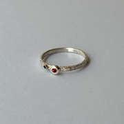 A silver ring with orange and blue sapphires set on the top, placed on a grey background.