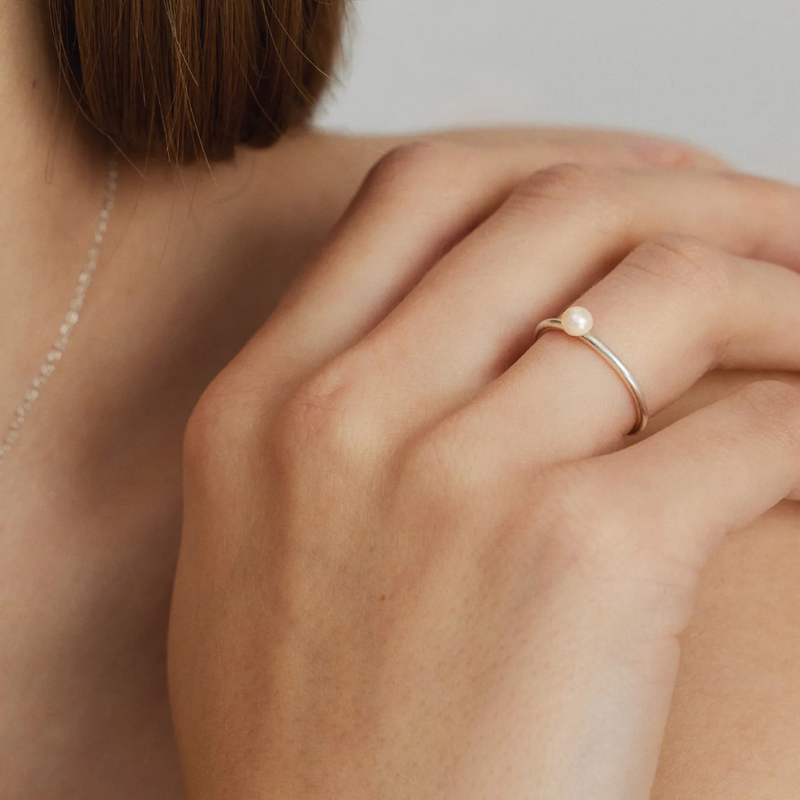 Close-up of a hand wearing a pearl ring on a neutral background