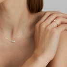 Close-up of a person wearing a silver necklace and gold ring on a neutral background