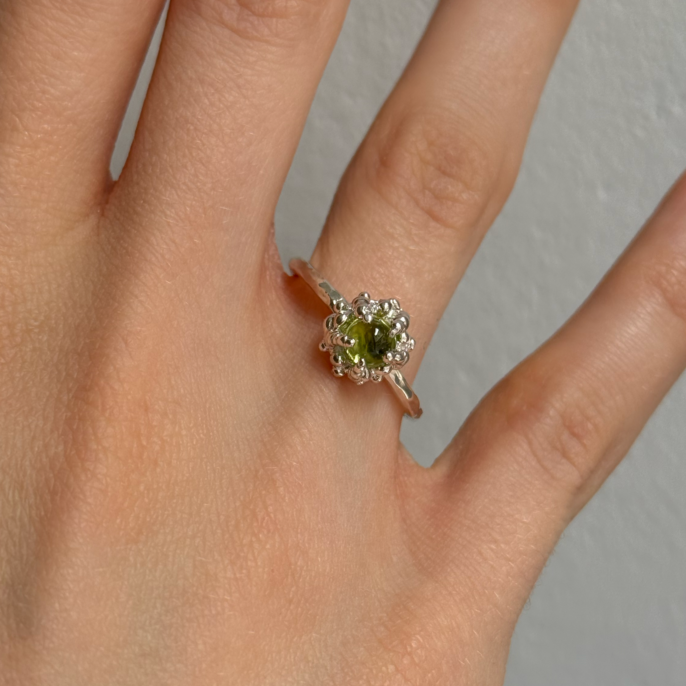 Hand wearing a silver ring with a green peridot on a neutral background