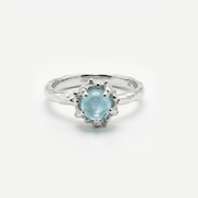 Silver ring with a light blue topaz on a white background