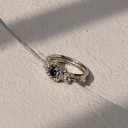 Silver ring with a green Moissanite on a textured white surface