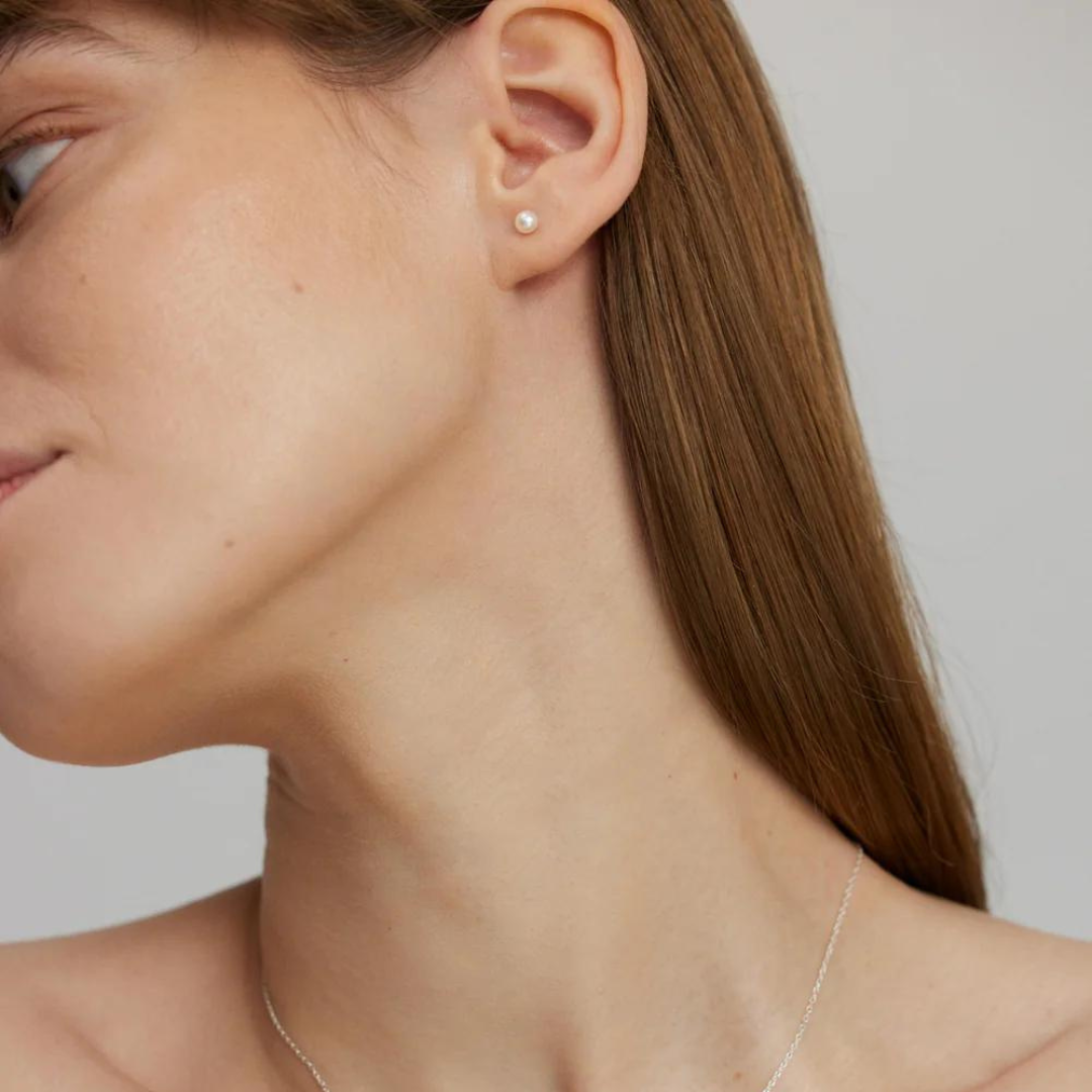 A woman wearing a single silver earring with a pearl, designed to be subtle and elegant.