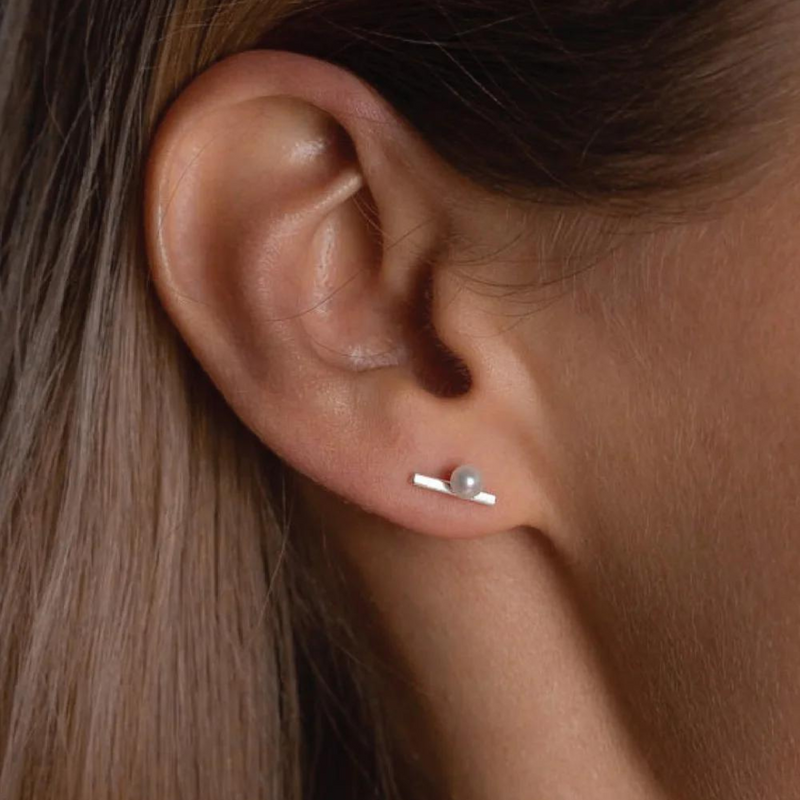 A silver stud earring with a round pearl attached to silver string.