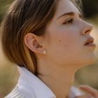 Close-up of a woman wearing a blue topaz earring with a blurred natural background
