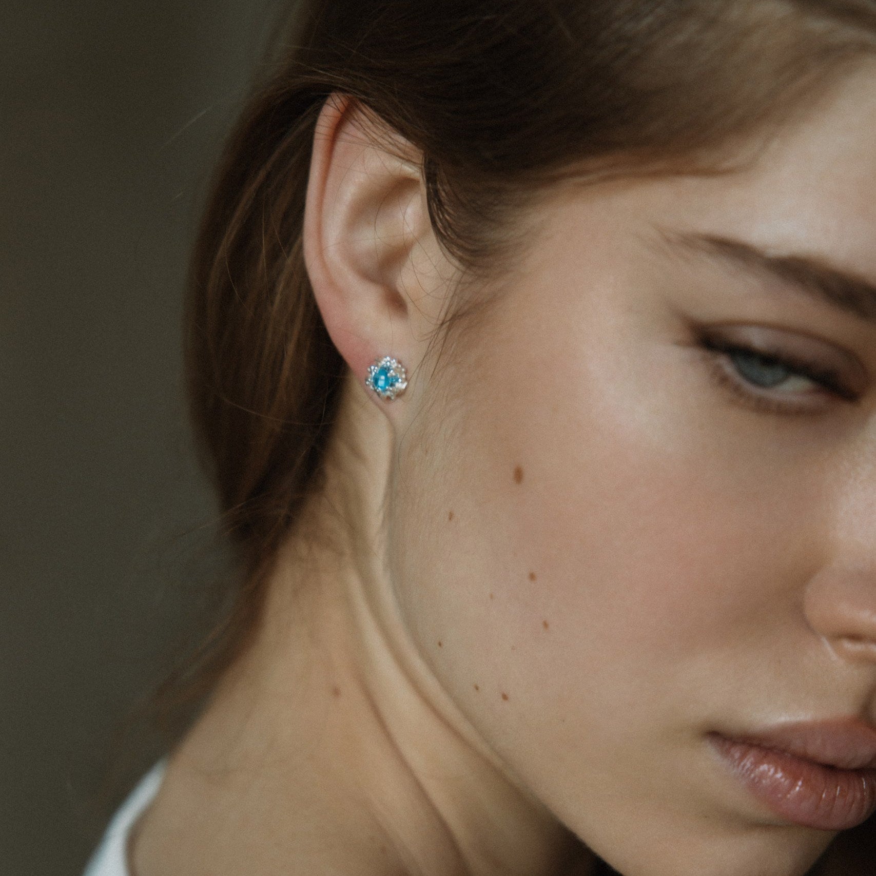 Close-up of a woman wearing a blue topaz earring with a blurred background