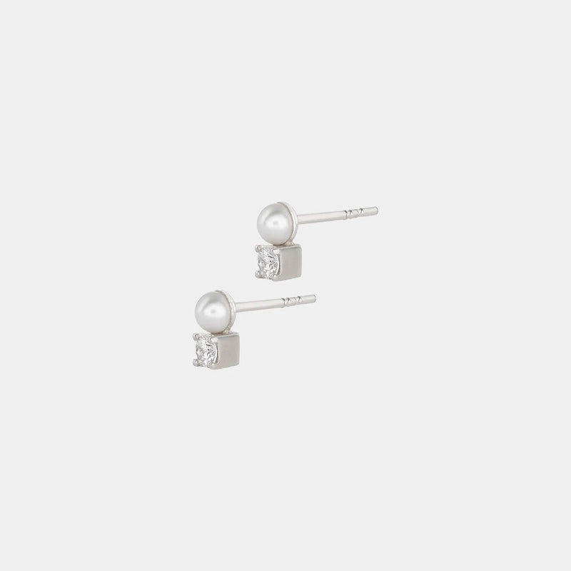 Pair of silver earrings with freshwater pearls and white zirconium stones on a light gray background