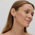 A woman wearing silver heart-shaped earrings that slantly fit close to the ear.