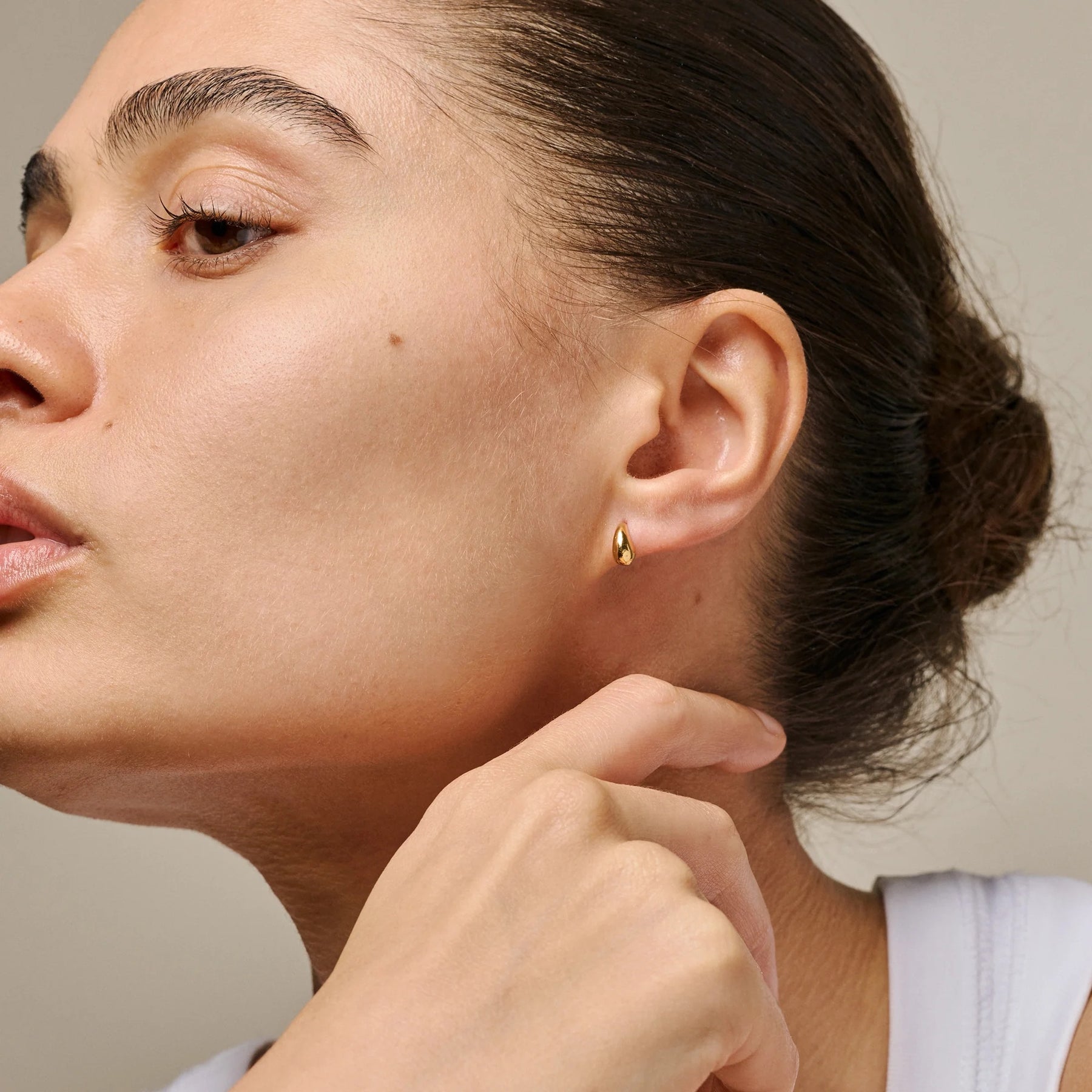 Close-up of a woman wearing a gold earring with a neutral background