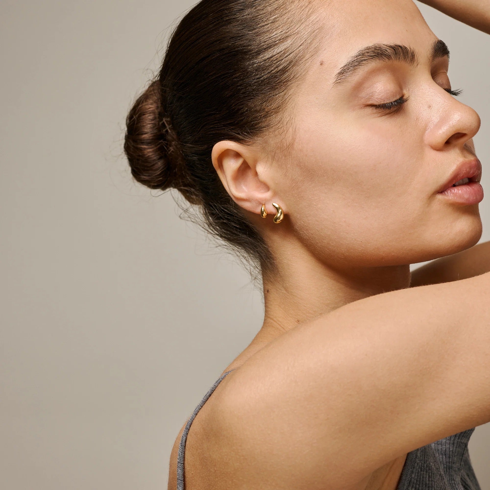 Woman wearing gold earrings against a neutral background