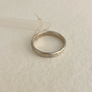 A polished thin silver ring with Latin inscription, displayed against a neutral background.