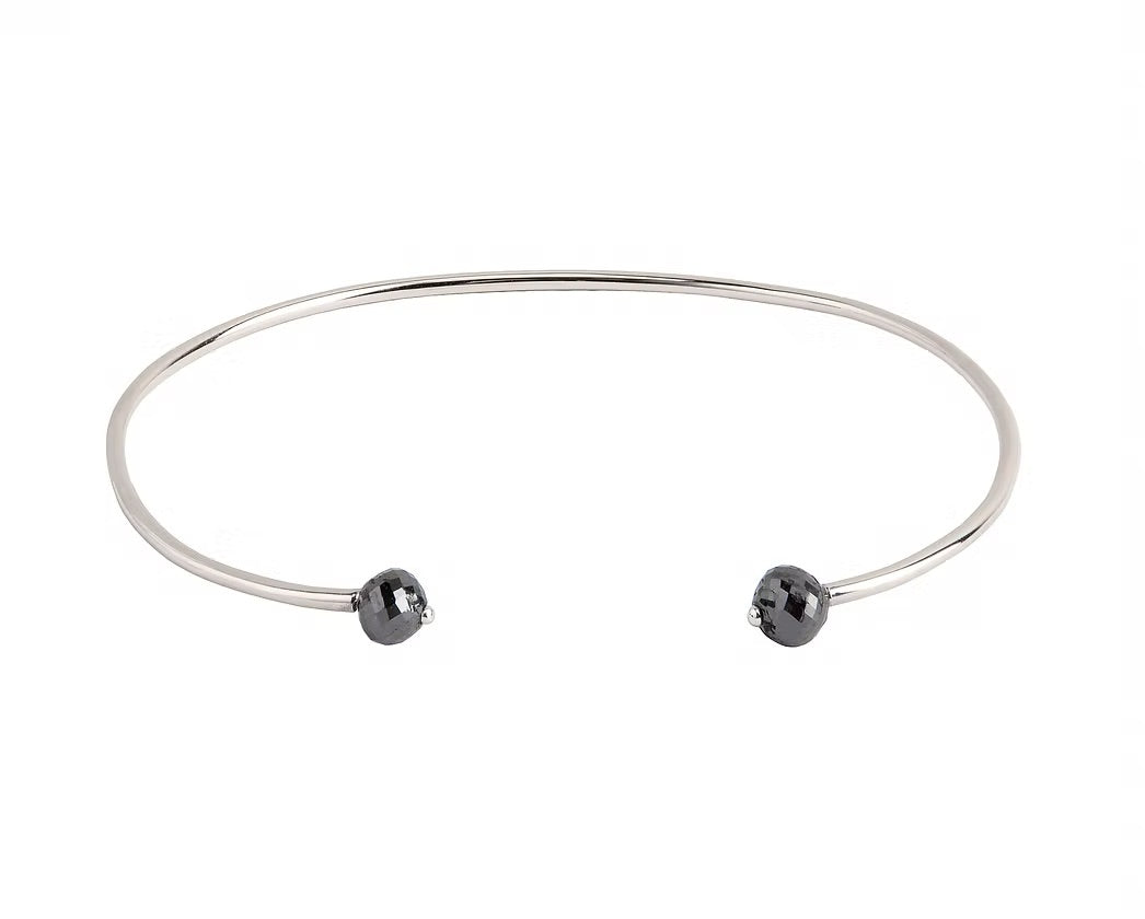A thin white gold open cuff bangle bracelet with two small faceted grey diamonds at the ends, shown on a plain white background.