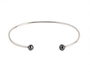 A thin white gold open cuff bangle bracelet with two small faceted grey diamonds at the ends, shown on a plain white background.